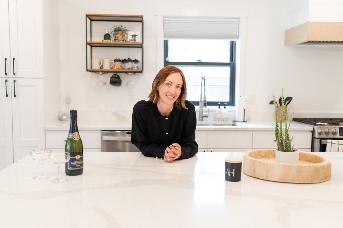 Amy smiling at a kitchen island with a bottle of champagne and two glasses