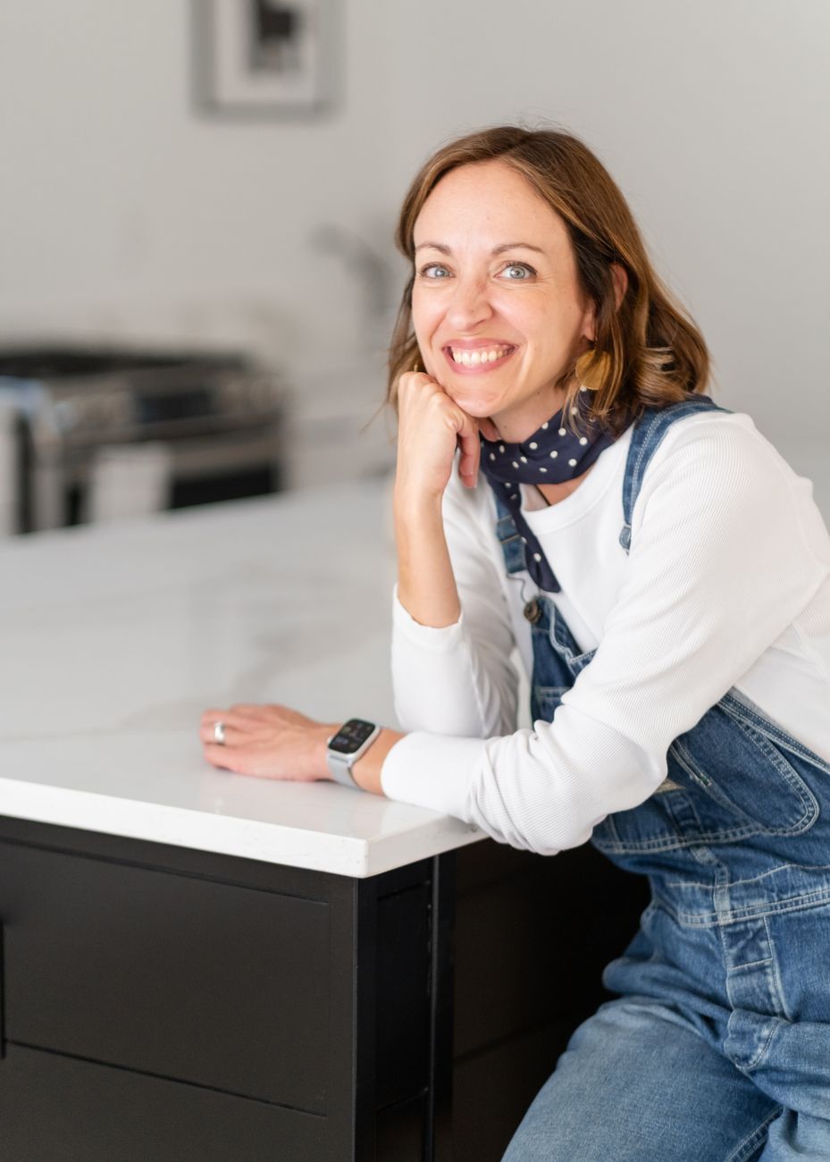 Amy in denim overalls smiling at a kitchen island