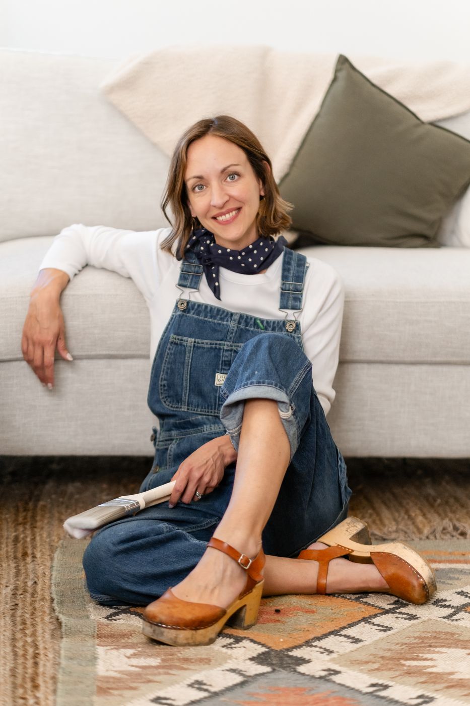 Amy in denim overalls sitting on a rug in front of a sofa