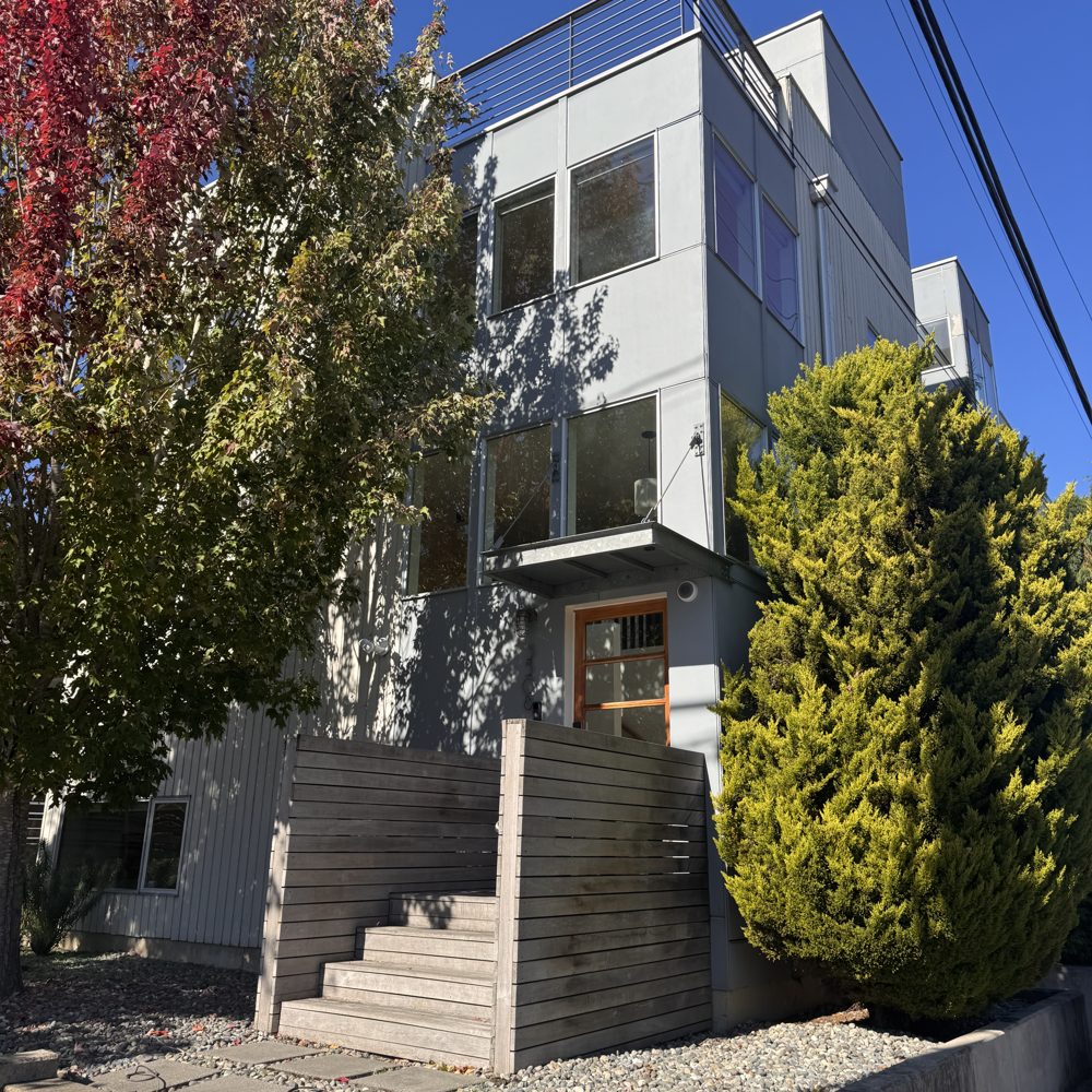 A modern three-story home with gray siding and concrete steps