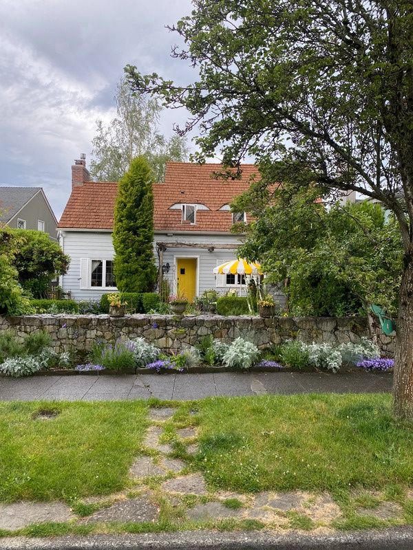 A cottage with a yellow front door behind a stone garden wall