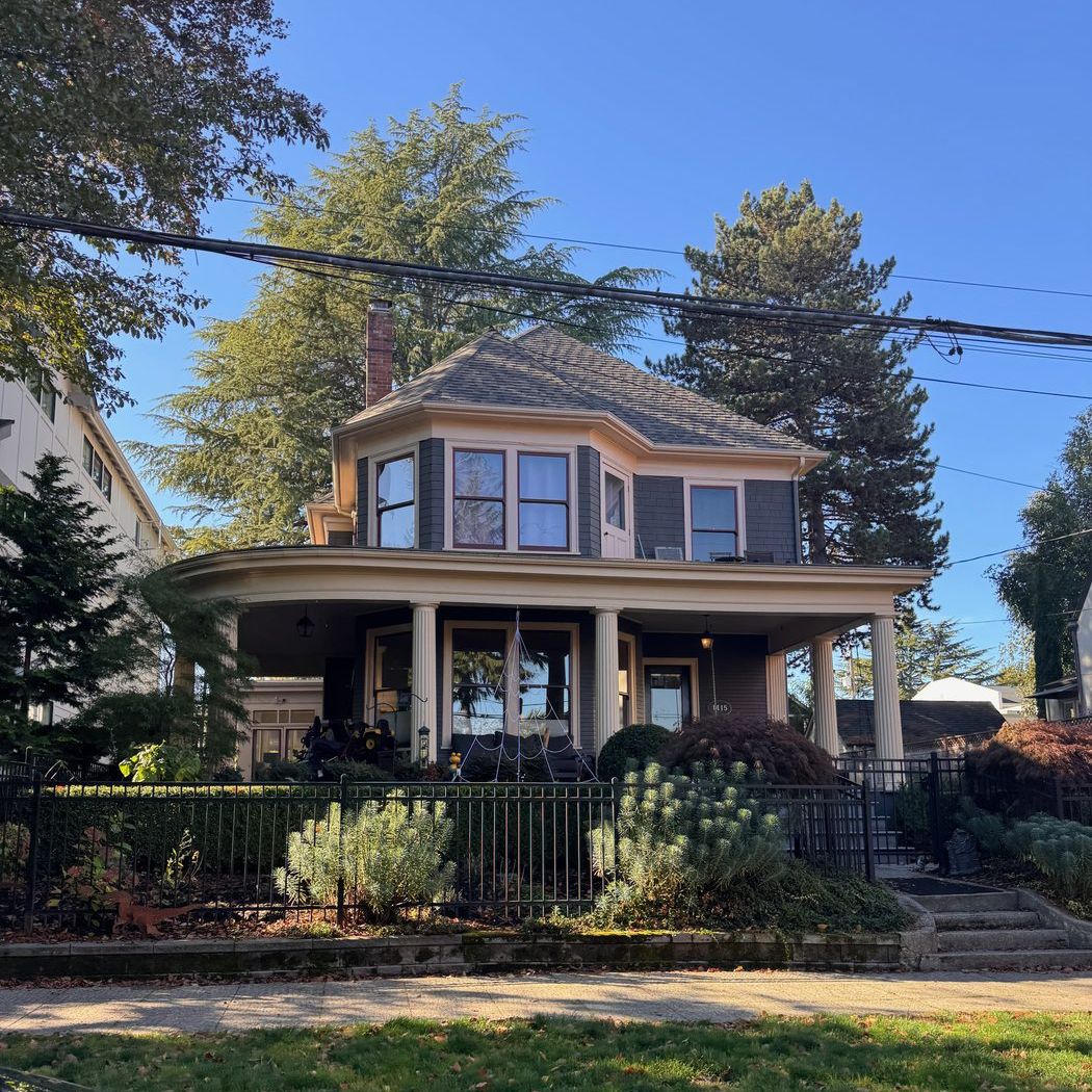 A Victorian-era home with a wraparound porch and a garden behind an iron fence