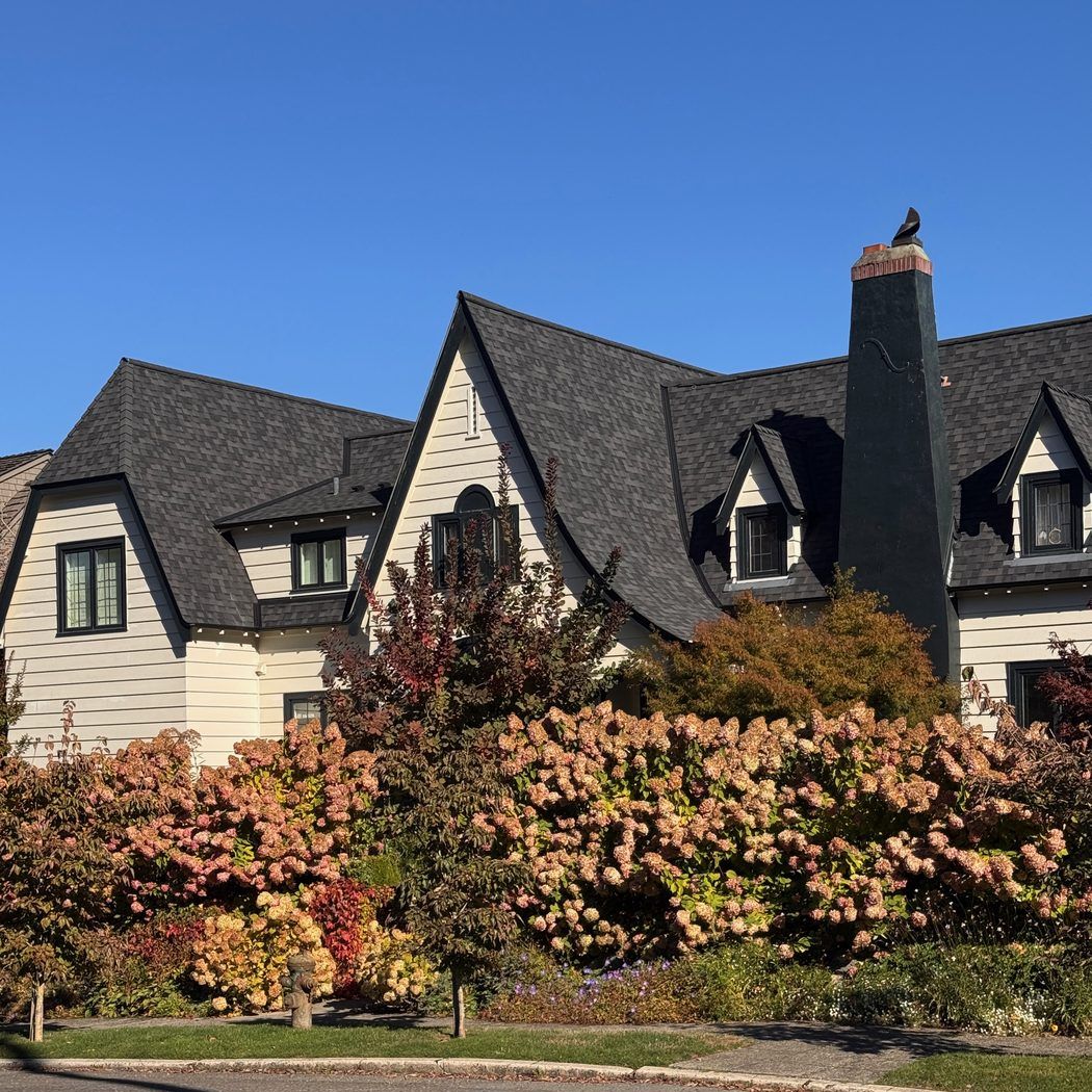 A storybook-style home with steep dark rooflines behind fall hydrangeas